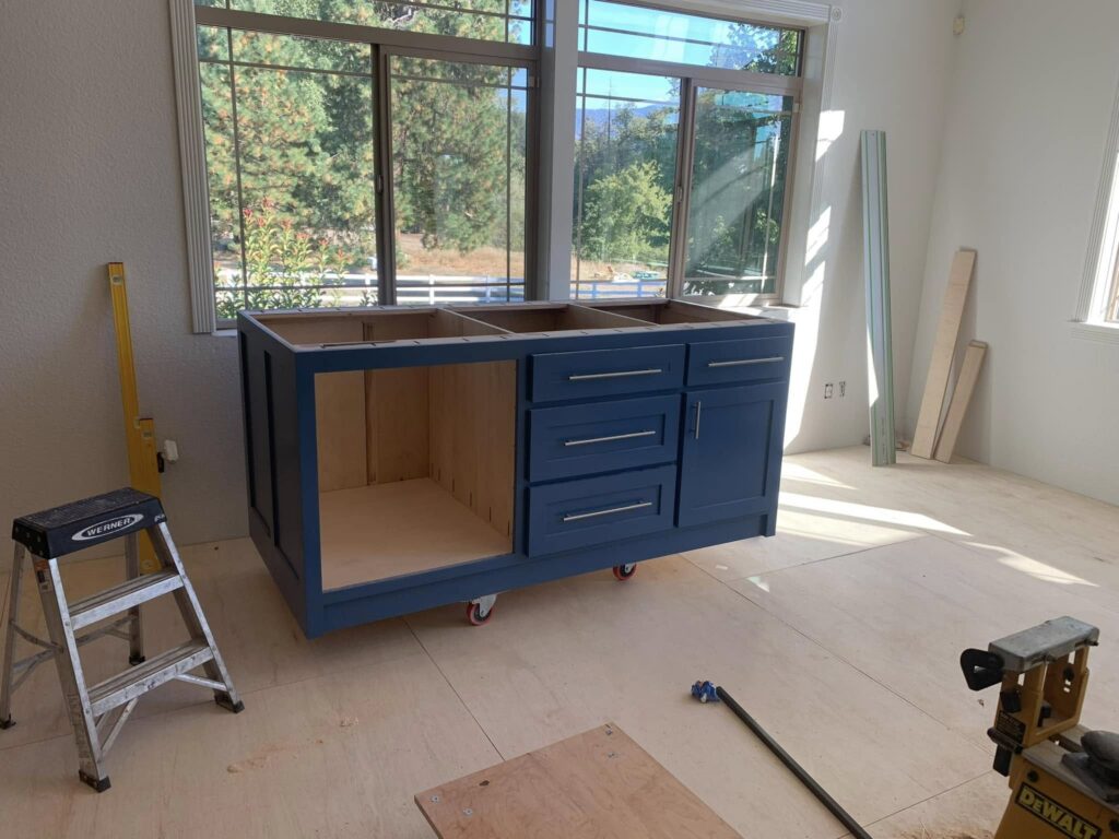 Blue bathroom vanity cabinet being installed beneath a window