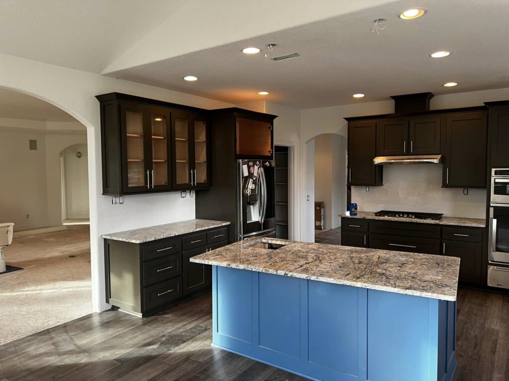 Finished kitchen with blue island, dark wall cabinets, and stone counters