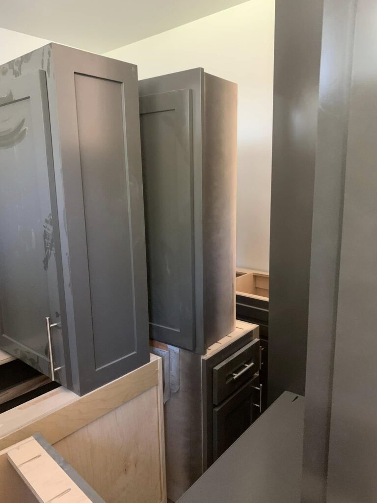 Tall gray pantry cabinet being installed beside an appliance