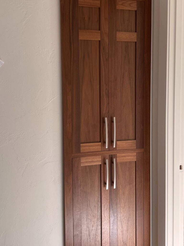 Tall walnut pantry cabinet installed in a doorway alcove