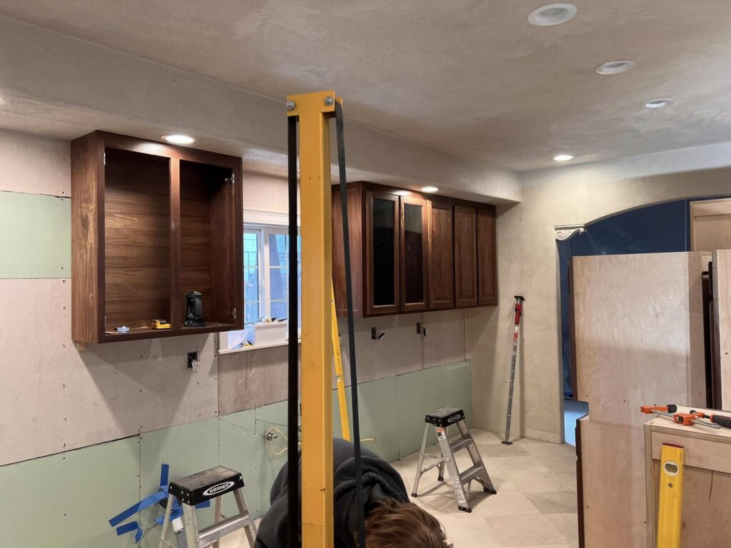 Walnut upper cabinets mounted during an active installation